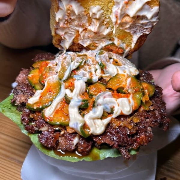 A Konjoe Burger with a smashed patty, pickles, and creamy sauce on a lettuce wrap.